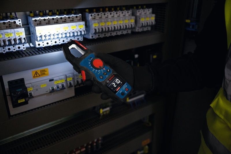 Oseba, ki nosi varnostno opremo, uporablja kleščni merilnik za preverjanje električne plošče.