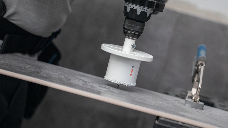 Oseba v varnostni opremi izvrta luknjo v keramični ploščici.