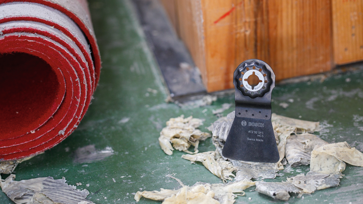 Oscilirajoče rezilo orodja stoji pokonci na zelenih tleh blizu rdeče zvite preproge.