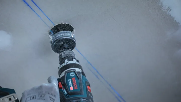 Oseba, ki nosi varnostno opremo, izvrta krožno luknjo v mavčno ploščo.