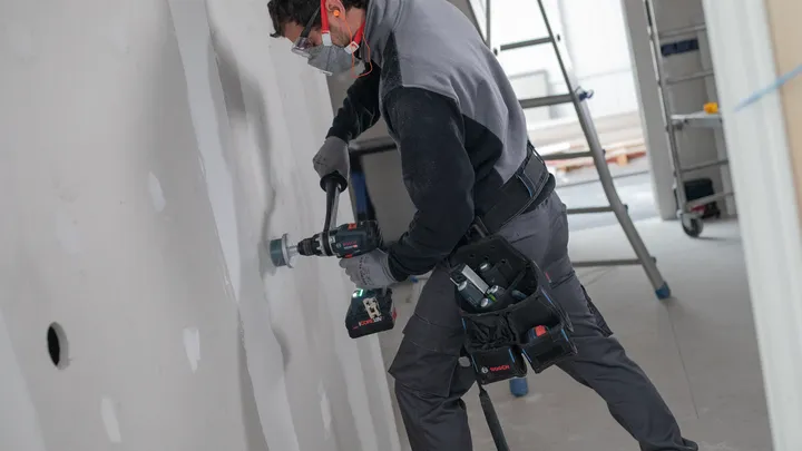 Oseba, ki nosi varnostno opremo, vrta v mavčno ploščo.