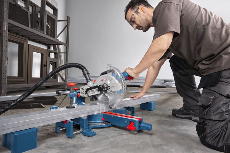 Oseba v varnostni opremi reže kovinski tram s kotno žago.