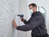 Oseba v varnostni opremi vrta v belo opečno steno.