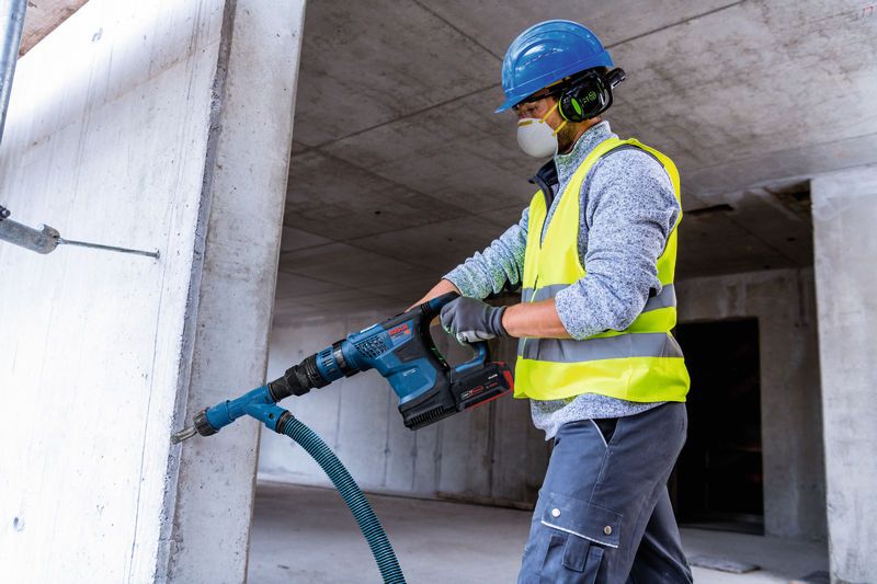 Delavec v varnostni opremi vrta v beton z akumulatorskim vrtalnim kladivom.