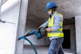 Delavec v varnostni opremi vrta v beton z akumulatorskim vrtalnim kladivom.