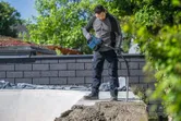 Oseba, ki nosi varnostno opremo, uporablja električno orodje za zbijanje betona na prostem.