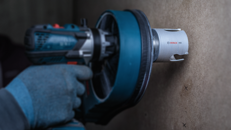 Oseba, ki nosi varnostno opremo, izvrta okroglo luknjo v mavčno ploščo.