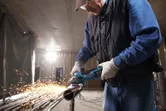 Osoba v bezpečnostnom vybavení brúsi kovovú rúru a vytvára iskry.