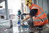 Osoba v bezpečnostnom vybavení obsluhuje diamantovú vŕtačku na mokrej betónovej podlahe.