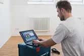 Osoba analyzuje údaje z termokamery na notebooku v miestnosti s radiátorom.