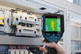 Osoba používa termokameru na kontrolu elektrických komponentov v ovládacom paneli.