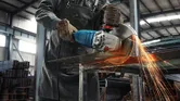 Osoba v bezpečnostnom vybavení reže plech veľkou uhlovou brúskou, pričom lietajú iskry.