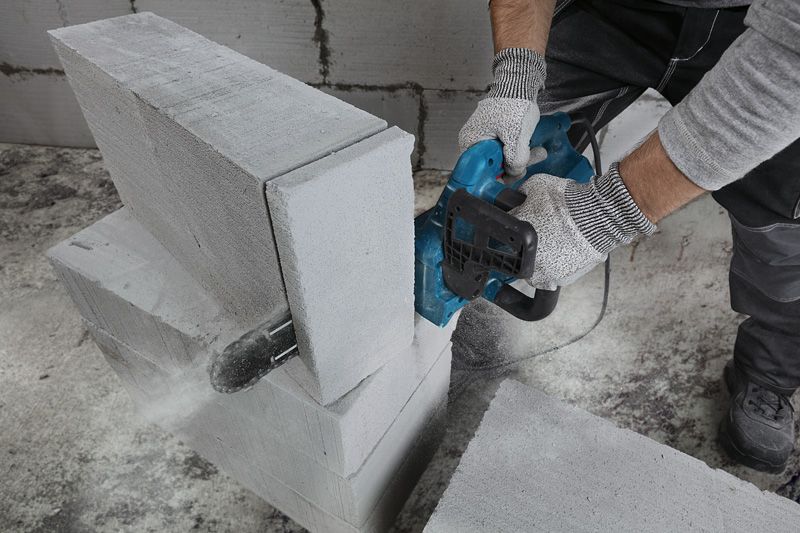 Osoba v bezpečnostnom vybavení reže AAC blok pomocou elektrickej rezačky.