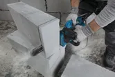 Osoba v bezpečnostnom vybavení reže AAC blok pomocou elektrickej rezačky.