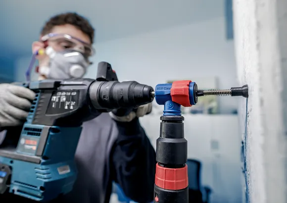 Osoba v bezpečnostnom vybavení vŕta do steny pomocou vŕtačky s príklepom.