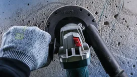 Pracovník v bezpečnostnom vybavení brúsi betónovú stenu elektrickým náradím.