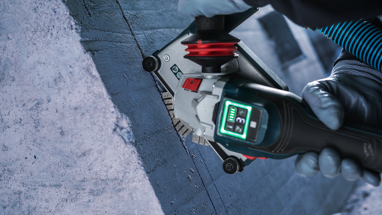 Osoba v bezpečnostnom vybavení obsluhujúca drážkovaciu frézu na betónovom povrchu.