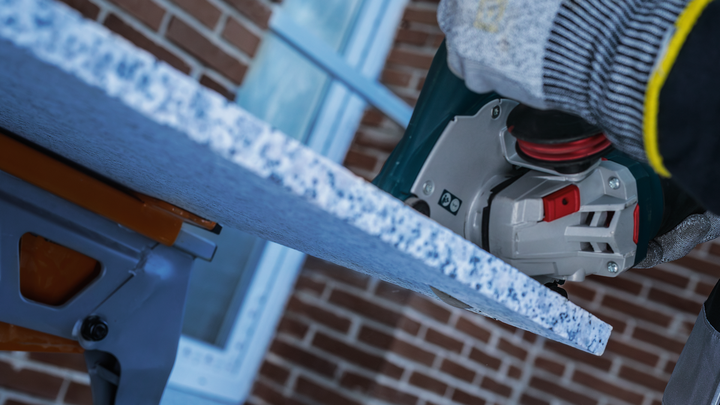 Osoba v bezpečnostnom vybavení používa motorovú pílu na rezanie kamennej dosky.