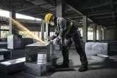 Osoba s ochranným vybavením používa uhlovú brúsku na kovovom potrubí na stavenisku.