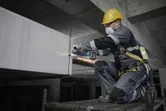 Osoba s bezpečnostným vybavením brúsi betón elektrickým náradím na stavenisku.