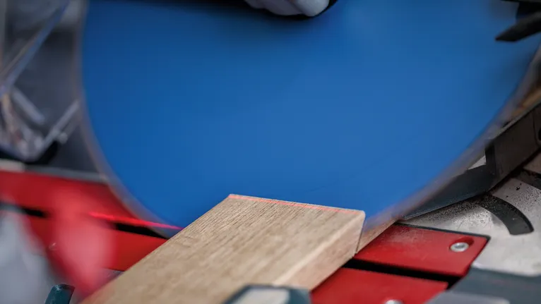 Osoba v bezpečnostnom vybavení reže drevenú dosku na kotúčovej píle.