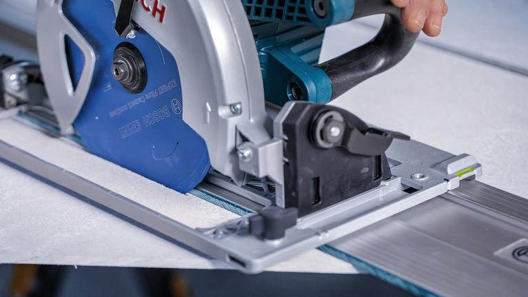 Osoba vedie kotúčovú pílu pozdĺž koľajnice, aby rezala dlaždicu.