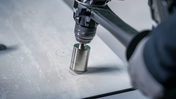 Osoba v bezpečnostnom vybavení vyvŕta kruhový otvor do betónového povrchu.