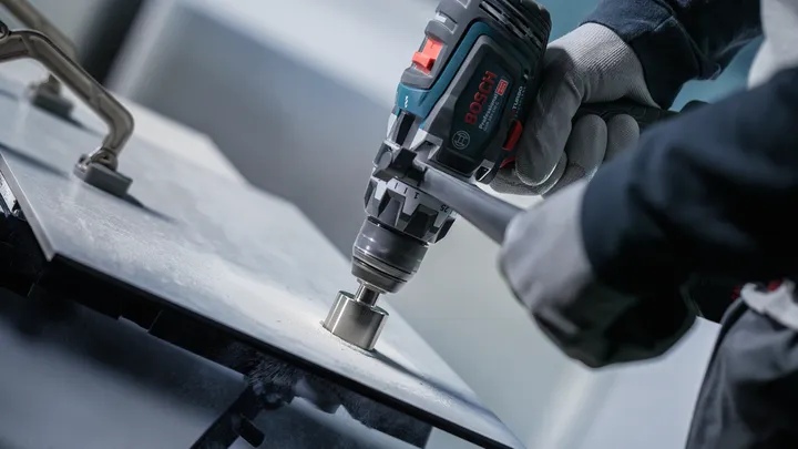 Osoba v bezpečnostnom vybavení vyvŕta dieru do dlaždicového povrchu.