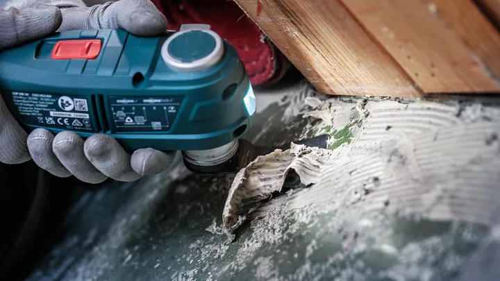 Osoba s ochranným vybavením odstraňuje zvyšky lepidla pomocou elektrického náradia.