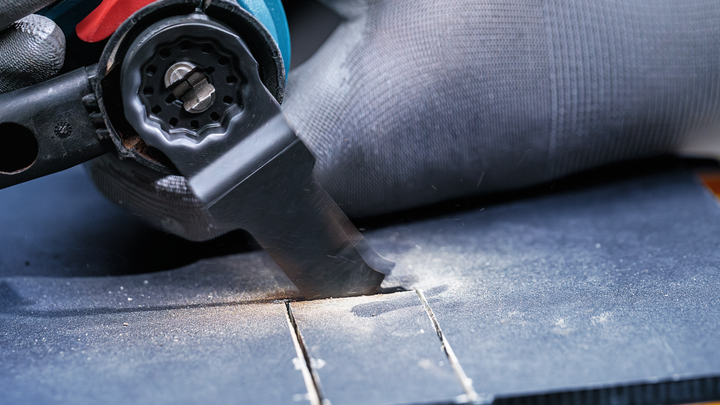 Osoba s ochranným vybavením používa elektrické náradie na vyrezanie drážky do dreva.