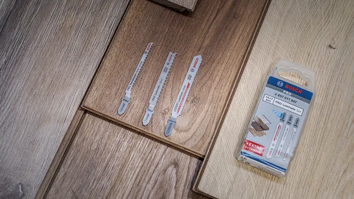 Tri listy priamočiarej píly a ich obal ležiace na drevenej laminátovej podlahe.