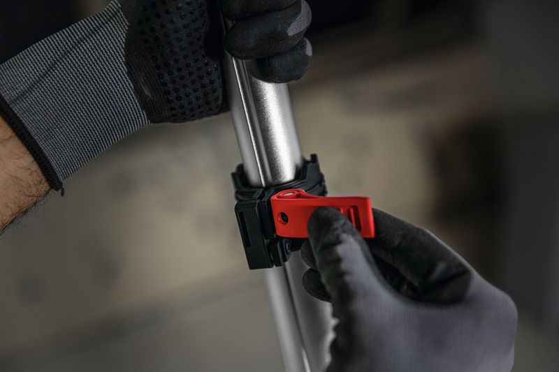 Osoba v bezpečnostnom vybavení nastavuje červenú svorku na kovovej tyči.