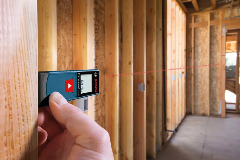 Person using a laser measure to check distance in a wooden framed room.