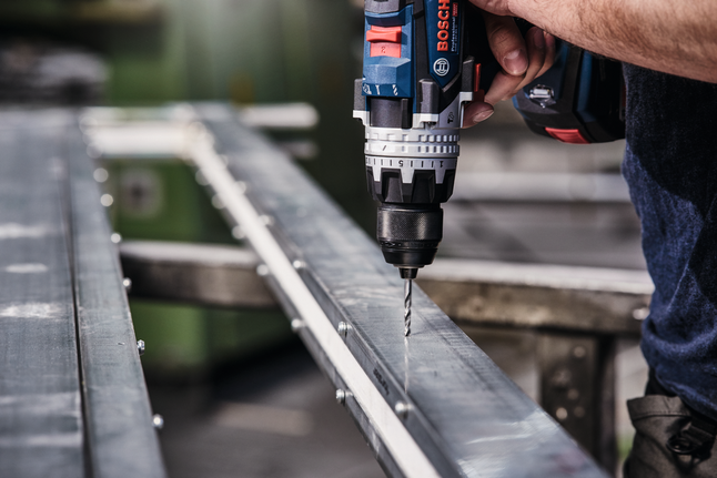 Cordless drill making a hole in a metal beam.