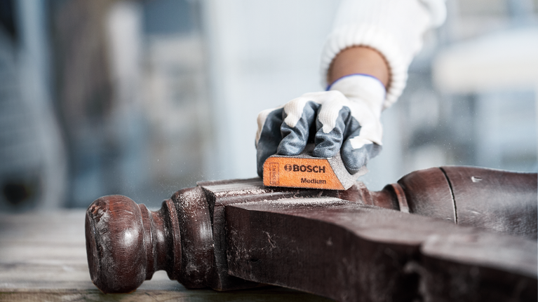Person wearing safety equipment sanding a wooden surface.