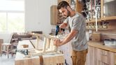 A person drills into a wooden frame on a workbench in a woodworking shop.