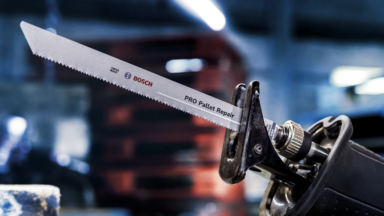 Reciprocating saw with a long blade attached, set in a warehouse workshop.