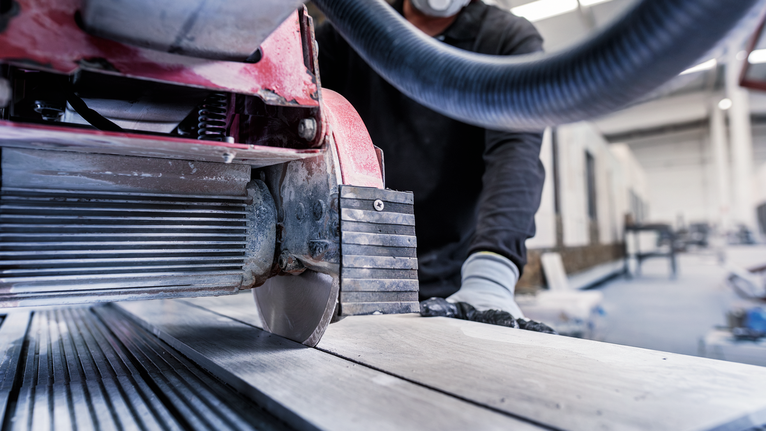 Person wearing safety equipment operates a tile saw to cut a ceramic slab.