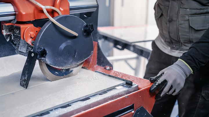 Person wearing safety equipment operating a tile saw to cut a large ceramic tile.