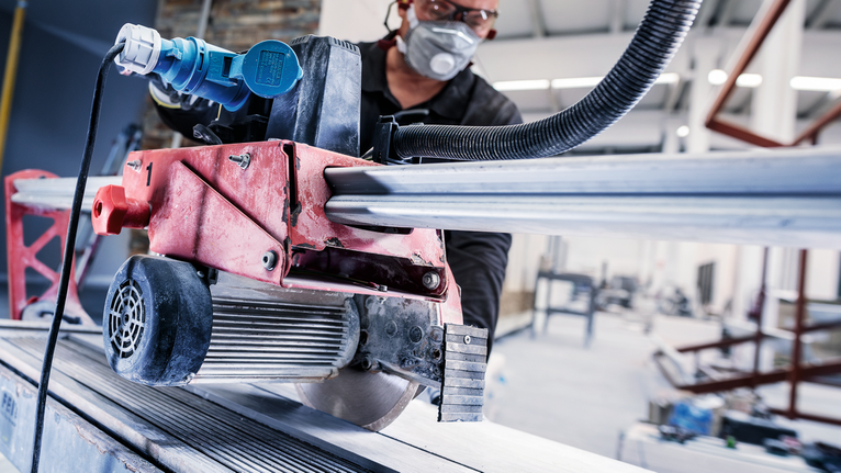 Person wearing safety equipment operates a circular saw to cut a metal beam.
