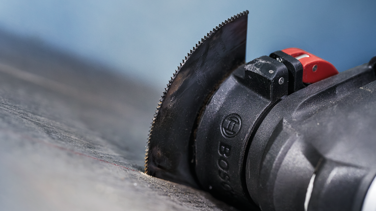 Oscillating multi-tool with a semicircular blade cutting into a wooden surface.