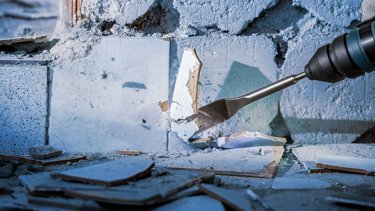 Chisel tool breaking wall tiles, creating rubble and debris on the ground.