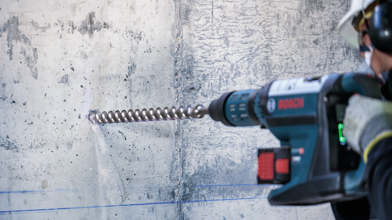 Person wearing safety equipment drills into a concrete wall with a rotary hammer.