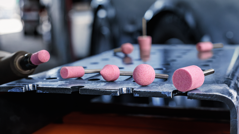 Pink grinding stones on a metal workbench beside a rotary tool.