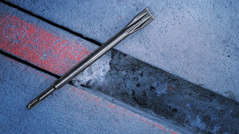 Flat chisel bit resting beside a narrow groove cut into a concrete surface.