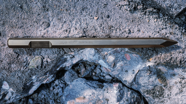 Pointed chisel lying on rough concrete rubble.