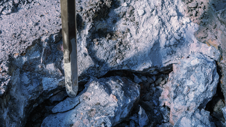 Chisel bit breaking apart rough stone in a construction setting.