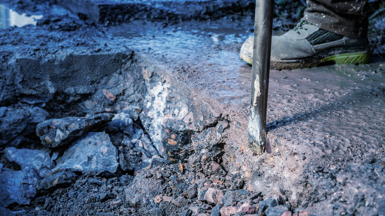 Person wearing safety equipment breaks concrete with a demolition tool.