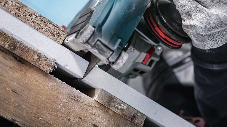 Person wearing safety equipment cuts a white board using a circular saw.