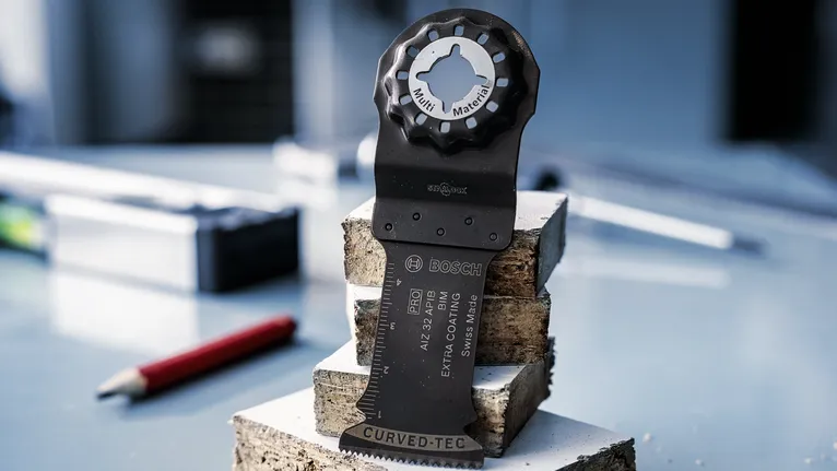 Oscillating multi-tool blade standing upright on stacked bricks, pencil and tools in background.